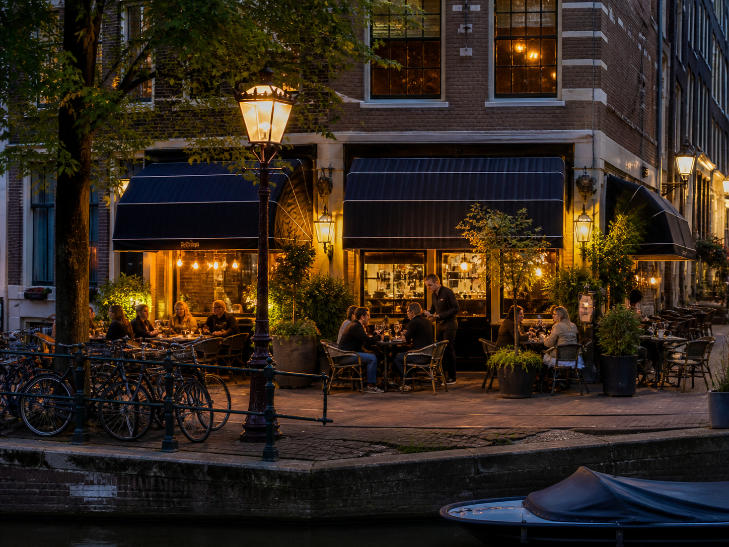 Terras van een grachtenpand in de avond, met gasten aan tafel en een medewerker die bedient